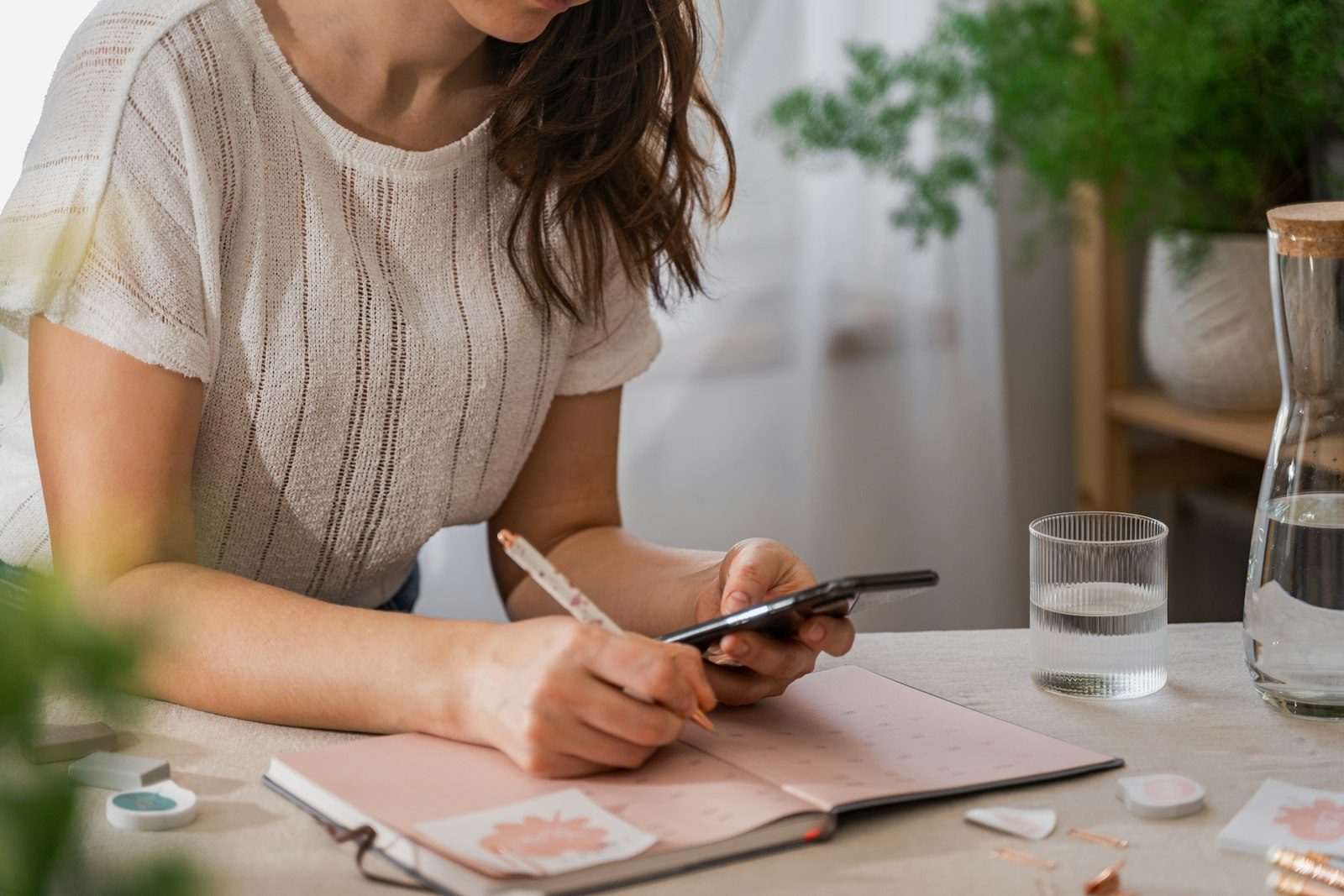 Frau notiert am Schreibtisch ihre Ausgaben, daneben ihr Smartphone